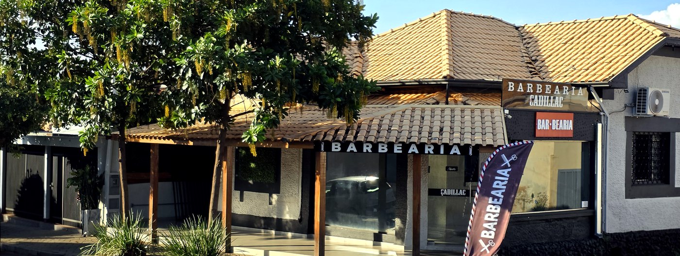 Fachada da Barbearia Cadillac em Olímpia com bandeira de barbearia na entrada