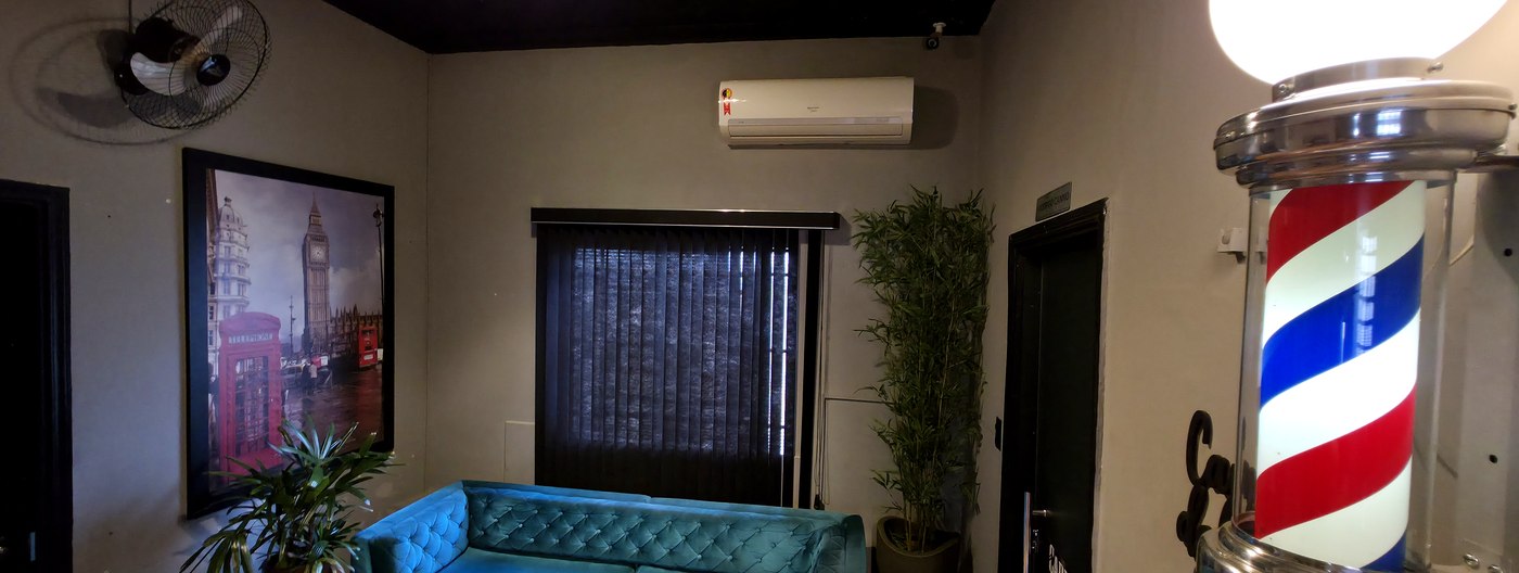 Sala de espera da Barbearia Cadillac com sofá verde e poste de barbeiro iluminado