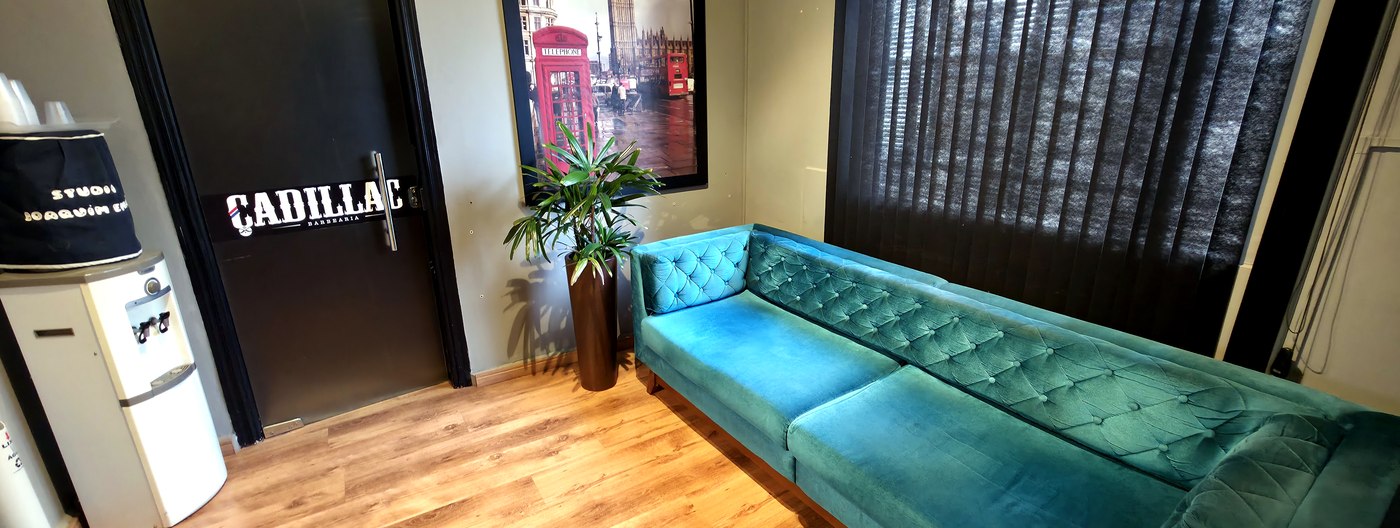 Sala de espera da Barbearia Cadillac com sofá verde e decoração vintage
